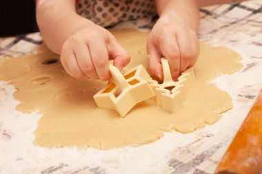 Masada kuru üzümlü ev yapımı kurabiyeler. Şekiller: Çember, yıldız, ağaç, kalp. Çocuk annesinin yemek yapmasına yardım ediyor.