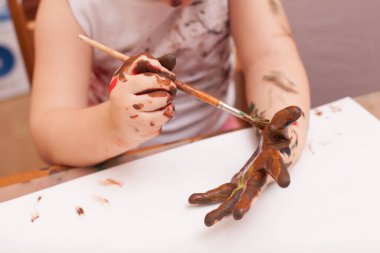 Kız masada oturuyor ve resim çiziyor. 