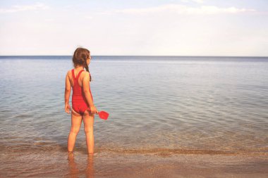 Kumsalda kırmızı mayolu genç ve güzel bir kız bulutlara bakıyor.