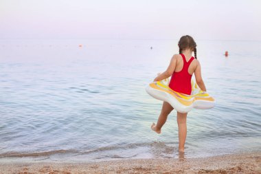 Kırmızı mayo giyen genç bir kız şişme donutla denizde yüzmeye gider.