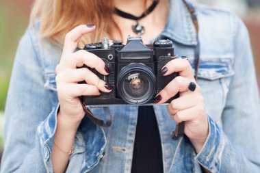 Sokakta eski bir kamerayla kot ceketle dolaşan genç bir fotoğrafçı kız.