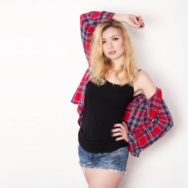 Beyaz duvarda poz veren güzel bir kız. Beyaz duvara karşı duran şort ve gömlekli.