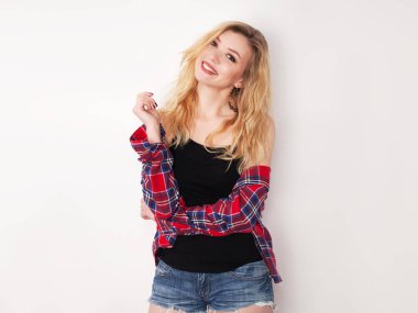 Beyaz duvarda poz veren güzel bir kız. Beyaz duvara karşı duran şort ve gömlekli.