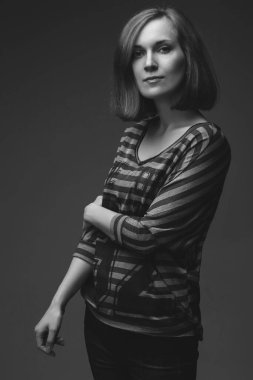 Güzel kız stüdyoda poz veriyor, kameraya bakıyor. Kızıl saç, mavi kot pantolon, gri bir arka plan, çizgili bir atlet. atlet üzerindeki metin değiştirildi