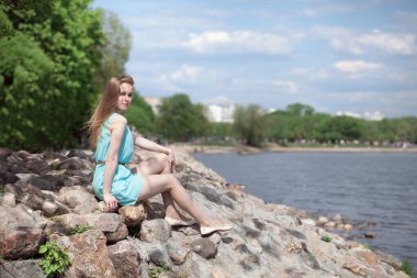 Genç, güzel sarışın kız kayalıklarda, nehir kıyısında oturuyor..