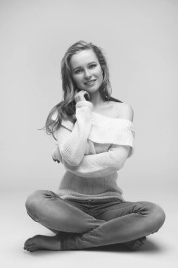 Güzel genç kız beyaz arka planda poz veriyor ve oturuyor. Beyaz kazaklı sarışın..