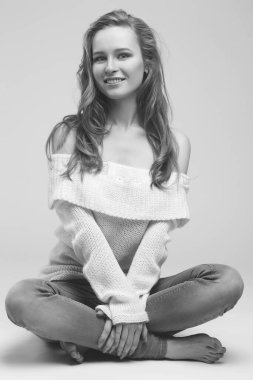 Güzel genç kız beyaz arka planda poz veriyor ve oturuyor. Beyaz kazaklı sarışın..