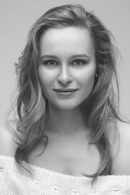 Güzel genç kız beyaz arka planda poz veriyor ve oturuyor. Beyaz kazaklı sarışın..