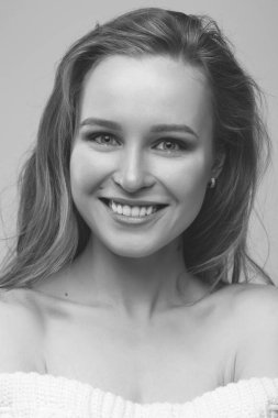 Güzel genç kız beyaz arka planda poz veriyor ve oturuyor. Beyaz kazaklı sarışın..