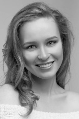 Güzel genç kız beyaz arka planda poz veriyor ve oturuyor. Beyaz kazaklı sarışın..