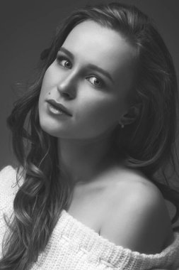 Güzel genç kız beyaz arka planda poz veriyor ve oturuyor. Beyaz kazaklı sarışın..