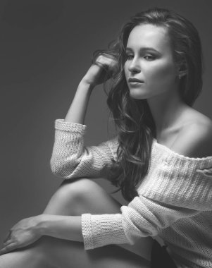 Güzel genç kız beyaz arka planda poz veriyor ve oturuyor. Beyaz kazaklı sarışın..