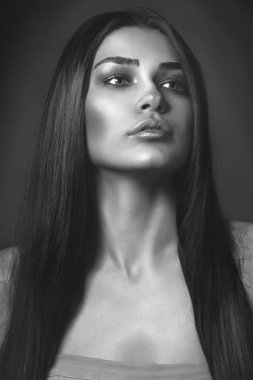 Güzel kız stüdyoda gri arka planda poz veriyor. Moda portresi. Makyaj malzemesi. Uzun saçlı. Siyah beyaz fotoğraf. 