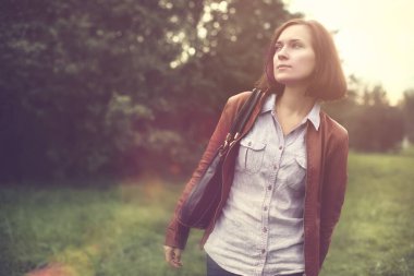 Güzel, şık kız yeşil ağaçlarla parkta yürüyor.