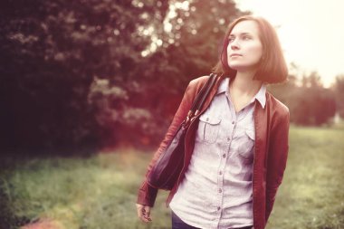 Güzel, şık kız yeşil ağaçlarla parkta yürüyor.