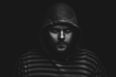 Siyah arka planda kapüşonlu bir adamın şeytani dramatik portresi.