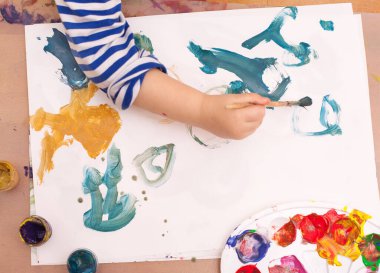 Yukarıdan bak. Çocuk bir fırça çizer ve beyaz kağıda resim yapar.