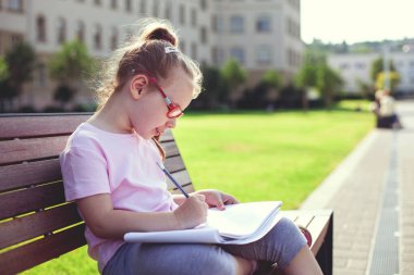 Gözlüklü genç bir kız bankta oturur ve albümde boyama, açık hava eğlencesi, sessizlik ve kendini geliştirme ile çizim yapar.
