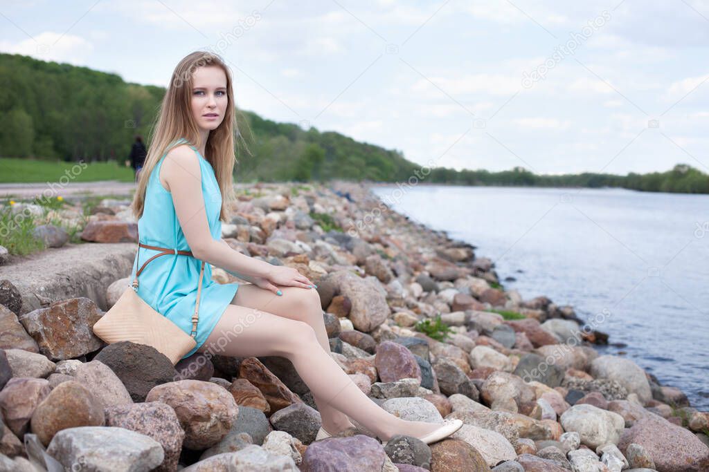 young beautiful blonde girl sitting on the rocks, on the river bank.