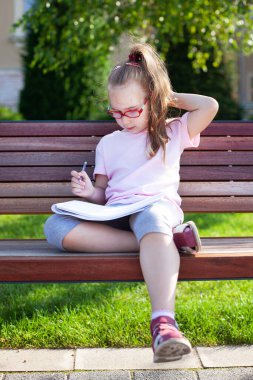 Gözlüklü kız dışarıda defterine yazıp çiziyor. ev ödevi.