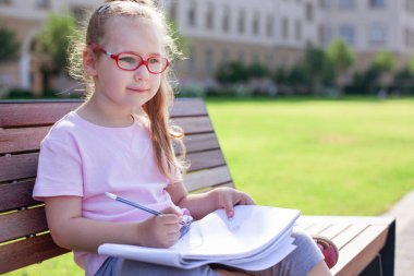 Gözlüklü kız dışarıda defterine yazıp çiziyor. ev ödevi.