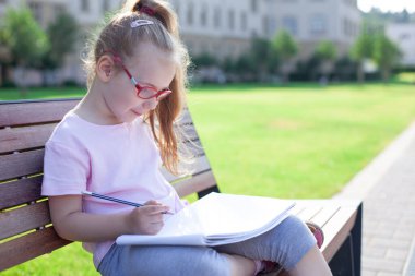 Gözlüklü kız dışarıda defterine yazıp çiziyor. ev ödevi.