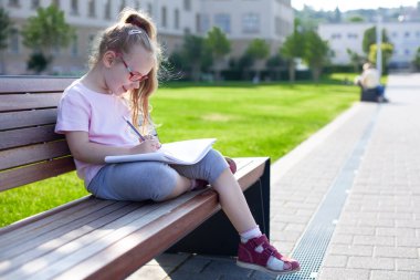 Gözlüklü kız dışarıda defterine yazıp çiziyor. ev ödevi.