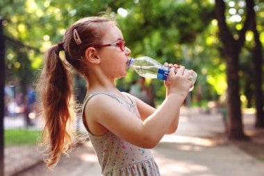 Gözlüklü genç kız güneşli bir günde parkta su içer.