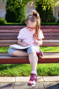 Gözlüklü kız dışarıda defterine yazıp çiziyor. ev ödevi.