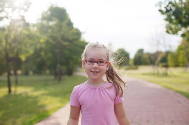 Genç kız parkta yol boyunca koşuyor. Parlak güneşli bir gün