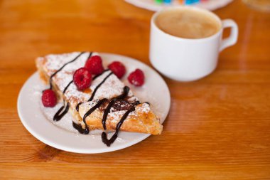 Pudra şekerli elmalı turta, taze ahududu ve çikolatalı krema. Bir fincan sade kahve.