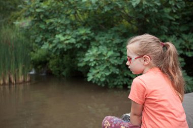 Genç kız köprüde oturur ve gölete bakar.