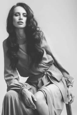 Stüdyoda poz veren güzel bir kız. Uzun kıvırcık siyah saçlar. yeşil-mavi elbise.