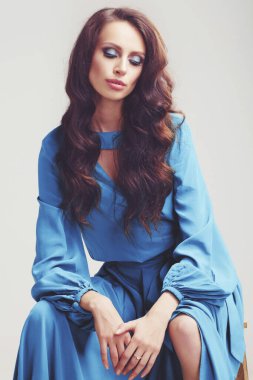 Stüdyoda poz veren güzel bir kız. Uzun kıvırcık siyah saçlar. yeşil-mavi elbise.