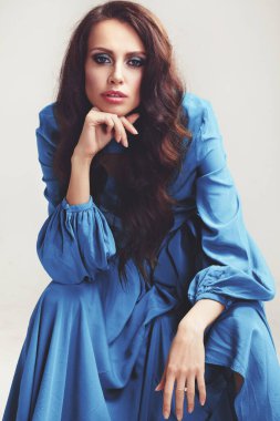 Stüdyoda poz veren güzel bir kız. Uzun kıvırcık siyah saçlar. yeşil-mavi elbise.