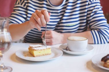 Çizgili elbiseli kız tatlıyla çatal yiyor ve kahve içiyor.