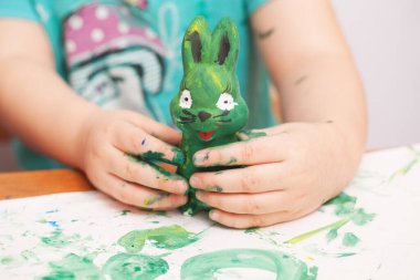 Çocuk yeşil boyalı bir tavşan figürü çiziyor.