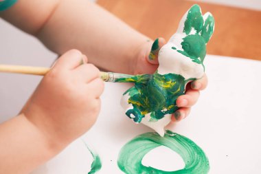 Çocuk yeşil boyalı bir tavşan figürü çiziyor.