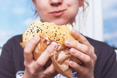 Kız büyük bir hamburger tutuyor. Yumuşak bulanık arkaplan. Yaşam tarzı
