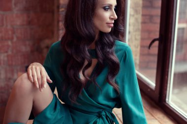 Genç güzel kız pencerenin yanında oturuyor. Bir elbisenin içinde romantik bir görüntü.