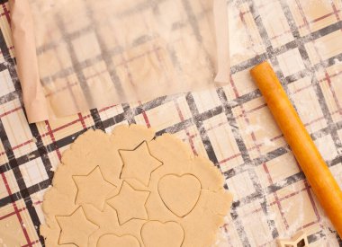 Masada kuru üzümlü ev yapımı kurabiyeler. Şekiller: Çember, yıldız, ağaç, kalp. Çocuk annesinin yemek yapmasına yardım ediyor.