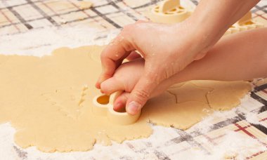 Masada kuru üzümlü ev yapımı kurabiyeler. Şekiller: Çember, yıldız, ağaç, kalp. Çocuk annesinin yemek yapmasına yardım ediyor.