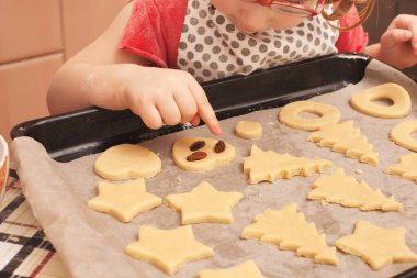 Masada kuru üzümlü ev yapımı kurabiyeler. Şekiller: Çember, yıldız, ağaç, kalp. Çocuk annesinin yemek yapmasına yardım ediyor.