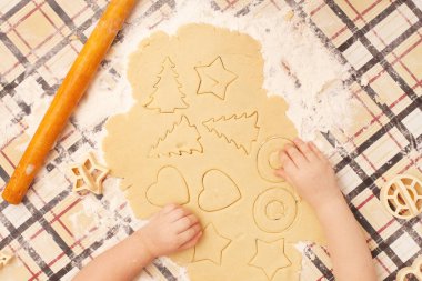 Masada kuru üzümlü ev yapımı kurabiyeler. Şekiller: Çember, yıldız, ağaç, kalp. Çocuk annesinin yemek yapmasına yardım ediyor.