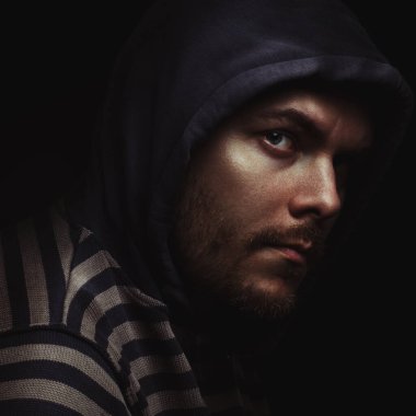 Siyah arka planda kapüşonlu bir adamın şeytani dramatik portresi.