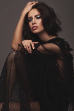 Siyah, seksi, şık elbiseli zayıf bir kız. Stüdyoda poz vermek. uzun siyah saçlar