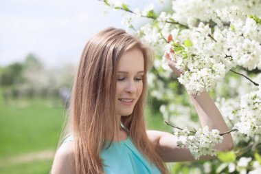 Mavi elbiseli genç sarışın bir kızın portresi. Çiçeklerdeki elma ağaçları.