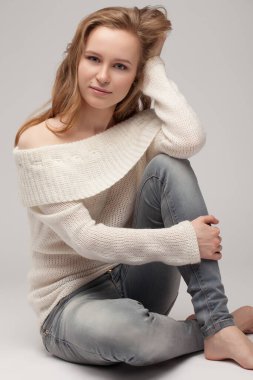 Güzel genç kız beyaz arka planda poz veriyor ve oturuyor. Beyaz kazaklı sarışın..