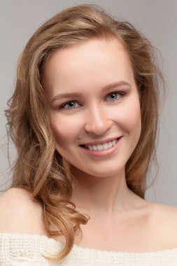 Güzel genç kız poz veriyor ve gülümsüyor. Beyaz kazaklı sarışın..