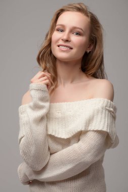 Güzel genç kız poz veriyor ve gülümsüyor. Beyaz kazaklı sarışın..